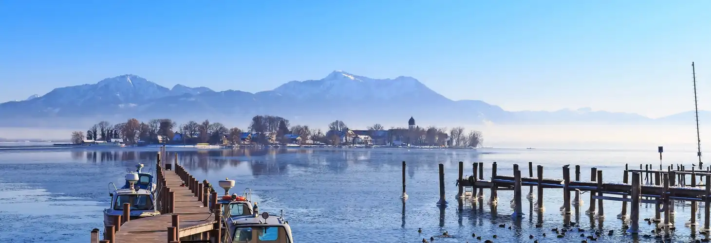 Boote an der Anlegestelle in Gstadt, Bayern, Deutschland, mit Blick auf die Fraueninsel an einem kalten Wintertag