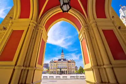 Blick durch einen Bogen auf ein historisches Gebäude mit Turm bei sonnigem Himmel.