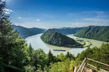 Flusslandschaft mit Wald und Schiff unter blauem Himmel.