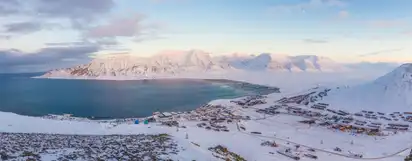 Verschneite Küstenlandschaft mit Bergen und Siedlung in Nordnorwegen.