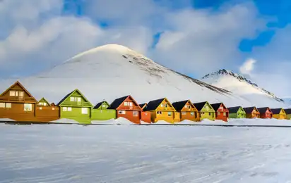 Bunte Holzhäuser vor schneebedecktem Berg im Winter.