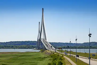 Hängebrücke über einen Fluss mit bewölktem Himmel im Hintergrund.