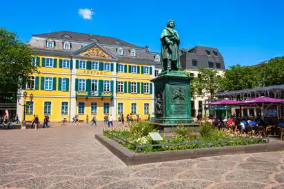 Statue und gelbes Gebäude auf einem belebten Platz mit blauem Himmel.
