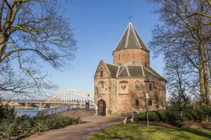 Historisches Backsteingebäude neben einer Brücke und Fluss in sonniger Landschaft.