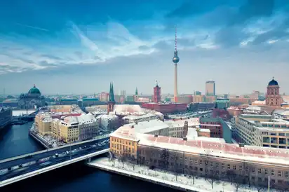 Winterliche Stadtansicht von Berlin mit Fernsehturm und verschneiten Dächern.