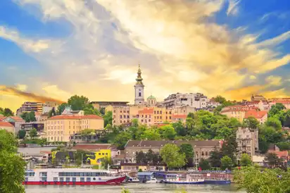 Stadtpanorama mit Fluss, Bäumen und alten Gebäuden bei Sonnenuntergang.