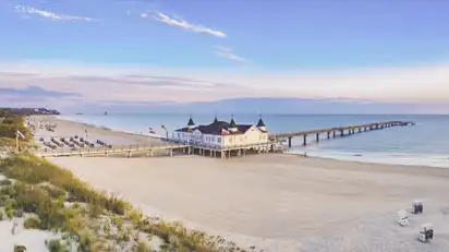 Strand mit Seebrücke und Gebäude im Hintergrund bei Sonnenuntergang.