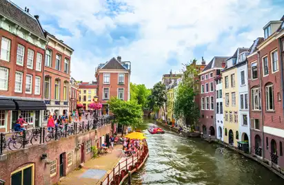 Kanal in einer Stadt mit Häusern, Bäumen und Menschen auf einer Terrasse.
