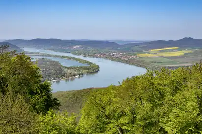 Landschaft mit Fluss und bewaldeten Hügeln unter blauem Himmel.