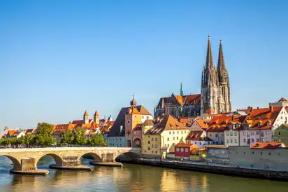 Stadtansicht mit Brücke und Kathedrale an einem Fluss bei Sonnenschein.