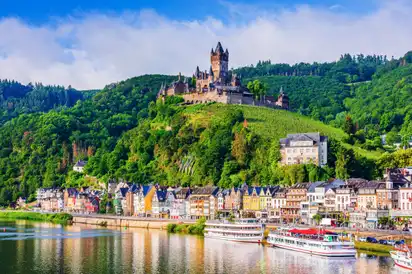 Stadt am Fluss mit Schloss auf Hügel, bunte Häuser und Boote.