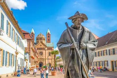 Statue eines Pilgers vor dem Speyerer Dom in einer belebten Fußgängerzone.