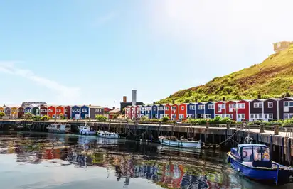 Bunte Häuser an einem Hafen mit Booten unter blauem Himmel.