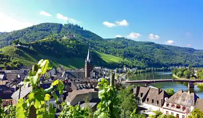 Stadtansicht mit Kirche und Hügeln im Hintergrund, Fluss im Vordergrund.