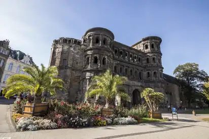 Alte römische Stadtmauer Porta Nigra in Trier, umgeben von Blumen und Palmen.