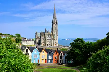 Bunte Häuser vor einer großen Kathedrale, im Hintergrund das Meer.
