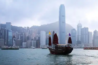 Traditionelles Segelschiff vor Hongkong-Skyline mit modernen Hochhäusern.