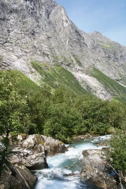 Tal mit bewaldeten Hängen und Bach, umgeben von steilen Bergen im Hintergrund.
