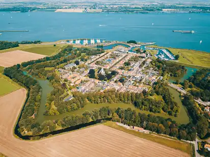Luftaufnahme einer befestigten Stadt mit Wasser und Feldern im Hintergrund.