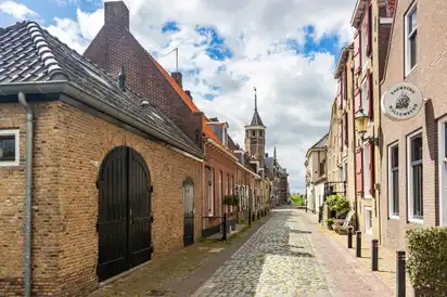 Pflastersteinstraße mit historischen Gebäuden und Kirchturm im Hintergrund.