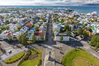 Blick auf die Küstenstadt Reykjavík mit bunten Häusern, Straßen und einem Hafen im Hintergrund.