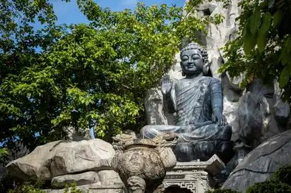 Buddha-Statue in einem Garten, umgeben von Bäumen und Felsen.