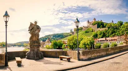 Statue auf einer Brücke mit Blick auf eine befestigte Burg und Hügel im Hintergrund.