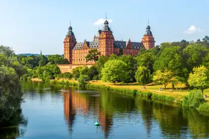 Schloss Johannisburg in Aschaffenburg, Bayern, am Fluss Main, umgeben von grüner Landschaft.