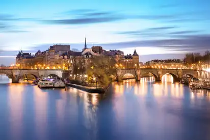 Brücke über die Seine in Paris, mit beleuchteten Gebäuden im Hintergrund bei Dämmerung.