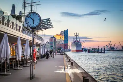 Hafenpromenade bei Sonnenuntergang mit Schiff und Elbphilharmonie im Hintergrund.