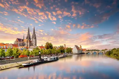 Städtische Flusslandschaft mit Kirche und Brücke im Sonnenuntergang.