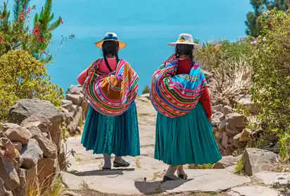 Zwei Frauen in traditioneller Kleidung gehen einen steinigen Weg zum See hinunter.