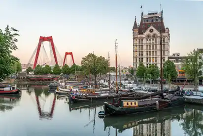 Boote im Hafen mit historischem Gebäude und Brücke im Hintergrund bei Sonnenuntergang.