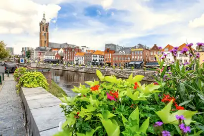 Blumen im Vordergrund, Kanal mit Brücke und Kirchturm im Hintergrund.