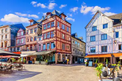 Historische Fachwerkhäuser an einem sonnigen Platz mit Cafés und blauem Himmel.