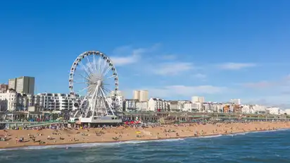 Riesenrad am Strand vor städtischer Kulisse bei klarem Himmel.