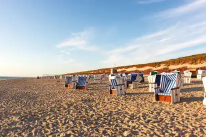 Sandstrand mit gestreiften Strandkörben unter blauem Himmel.