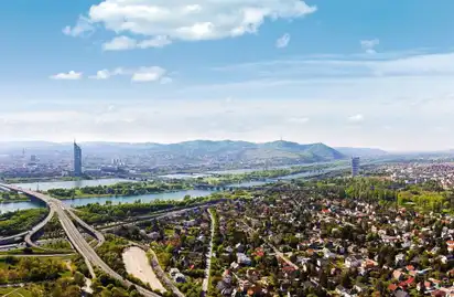 Luftaufnahme von Wien mit Donau, Stadt und umliegenden Hügeln bei klarem Himmel.