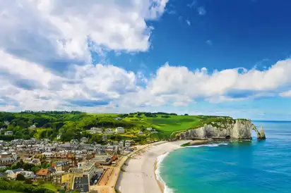 Küstenstadt mit Strand und Klippen unter blauem Himmel mit Wolken.