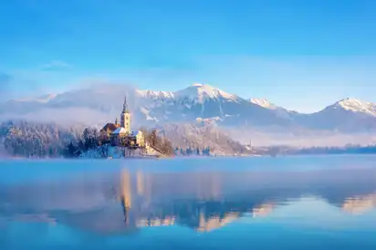 Kirche auf Insel im Bleder See mit Alpen im Hintergrund.