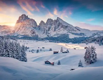 Winterliche Berglandschaft mit schneebedeckten Hütten im Sonnenuntergang.