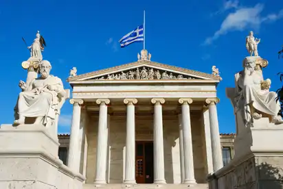 Neoklassisches Gebäude mit Säulen und griechischer Flagge bei blauem Himmel.