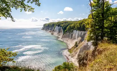 Kreidefelsen am Meer mit bewaldeter Küste und blauem Himmel.