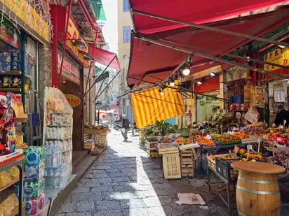 Marktstand in Palermo auf Sizilien mit verschiedenen Produkten, darunter Obst und Gemüse, unter roten Markisen.