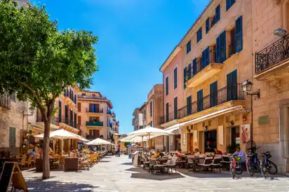 Straßencafé in einer sonnigen europäischen Altstadt mit Menschen und Fahrrädern.