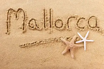 Mallorca im Sand geschrieben auf einem Strand mit zwei Seesternen.