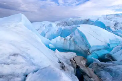 Gletscher mit blauen und weißen Eisschichten unter bewölktem Himmel.
