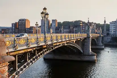 Brücke mit dekorativen Geländern und Laternen über einem Fluss, Stadthintergrund.