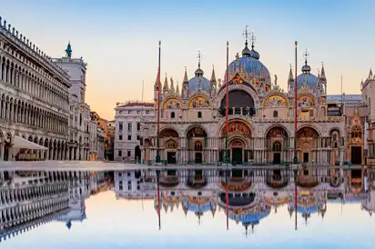 Basilika San Marco bei Sonnenaufgang mit Spiegelung im Wasser.