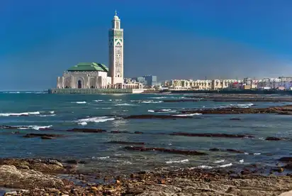 Hassan-II-Moschee an der Küste von Casablanca, mit blauem Himmel und Meer im Vordergrund.